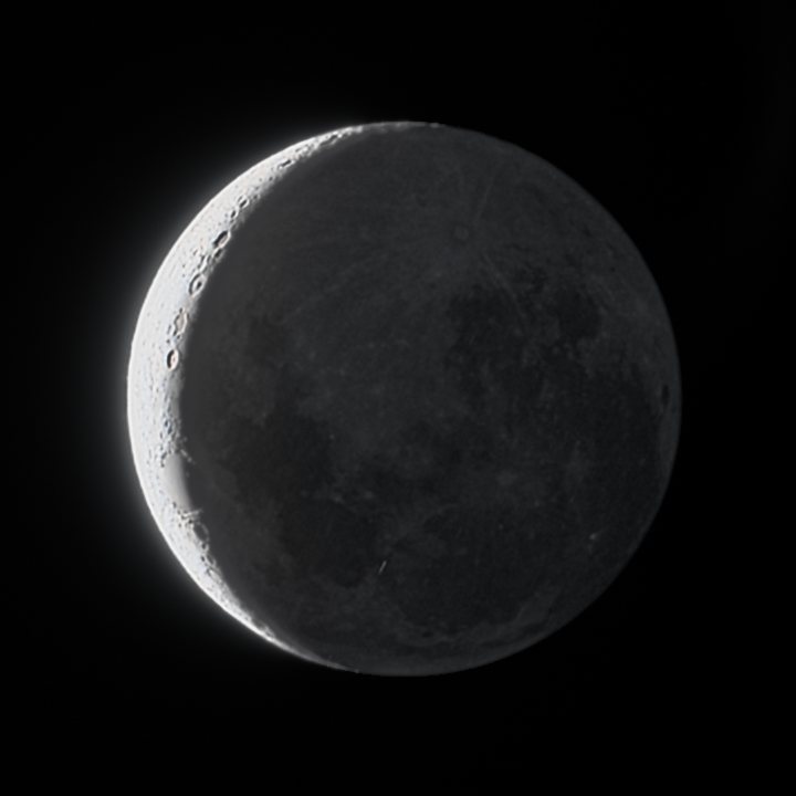 The same Moon with craters on the crescent and the dark seas visible on the softly lit dark side